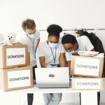 Guy and girl with check boxes. Volunteers in masks with laptop. Boxes with humanitarian aid.